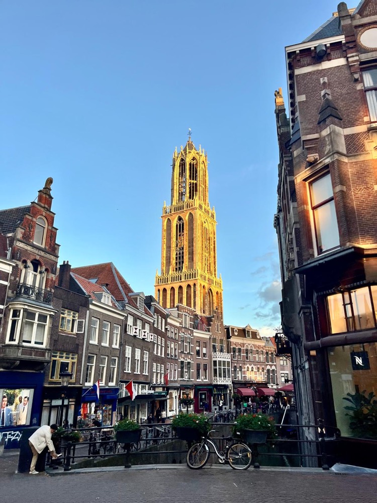 De Domtoren van Utrecht in avondlicht, met grachtenpanden en een fiets op de voorgrond